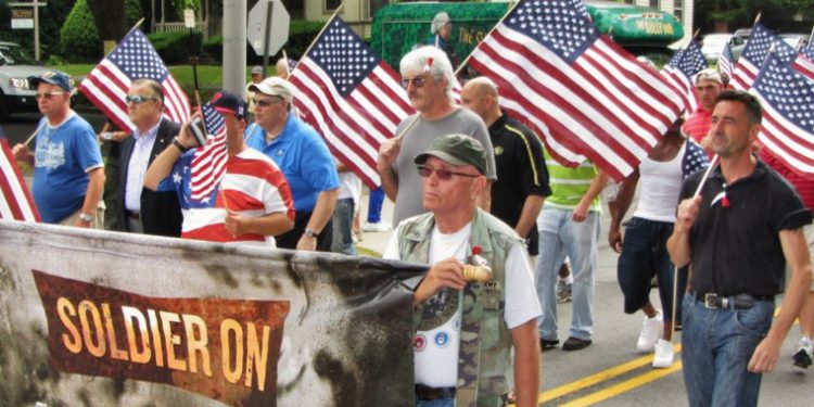 Image of men in a parade with American flags marching for Soldier On. 